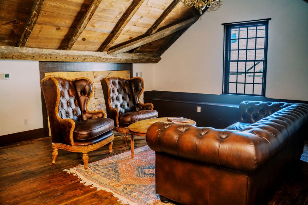 Luxurious attic lounge with brown leather wingback chairs and Chesterfield sofa on hardwood floors.