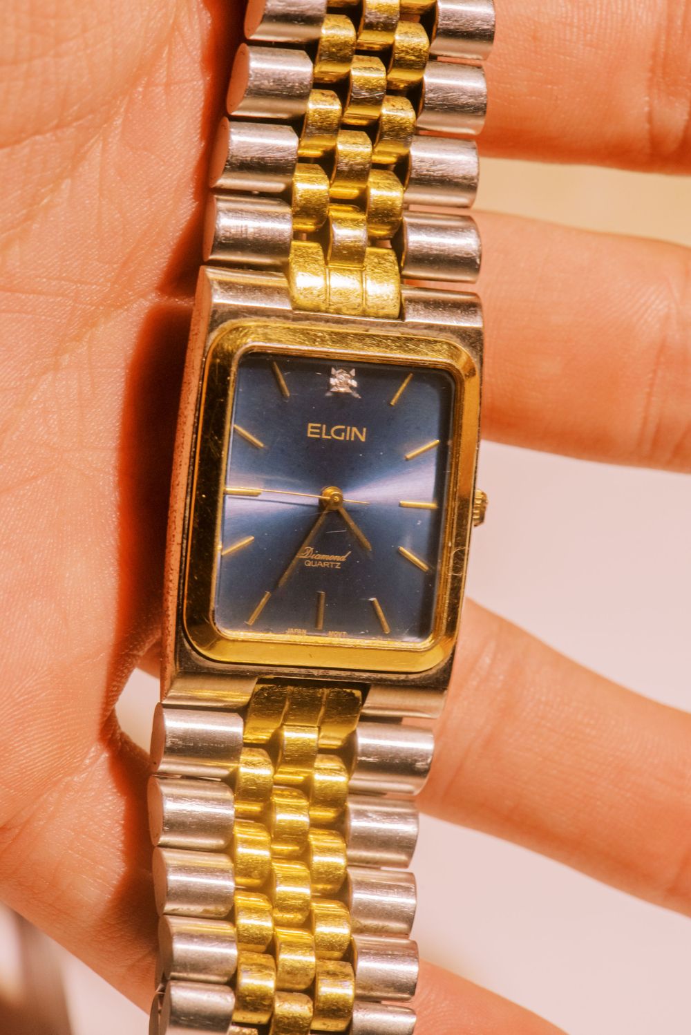 Close-up of a two-tone Elgin watch with gold and silver metal band against a skin-toned background.