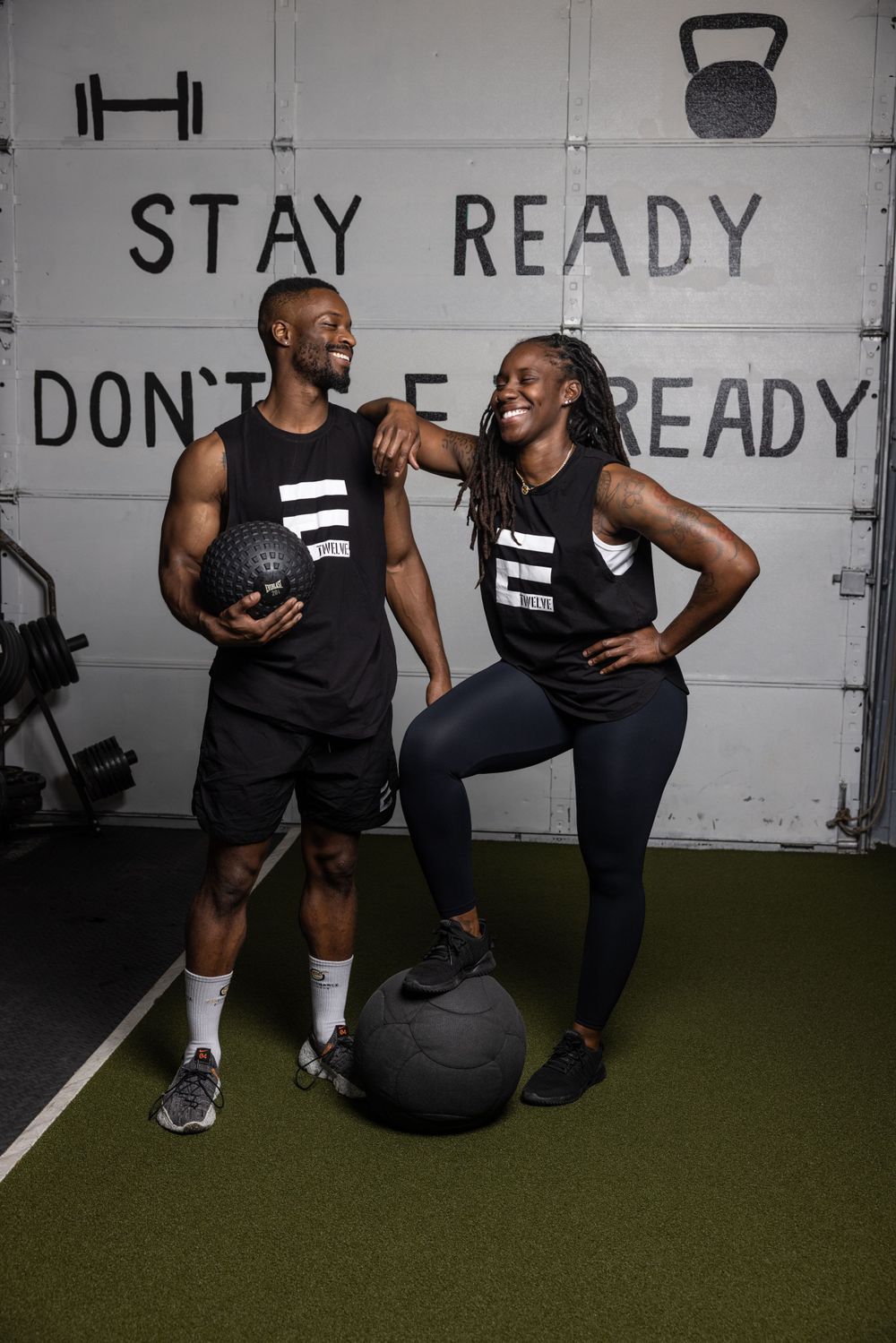 Fitness trainers demonstrate exercises with medicine ball against white wall with motivational text.