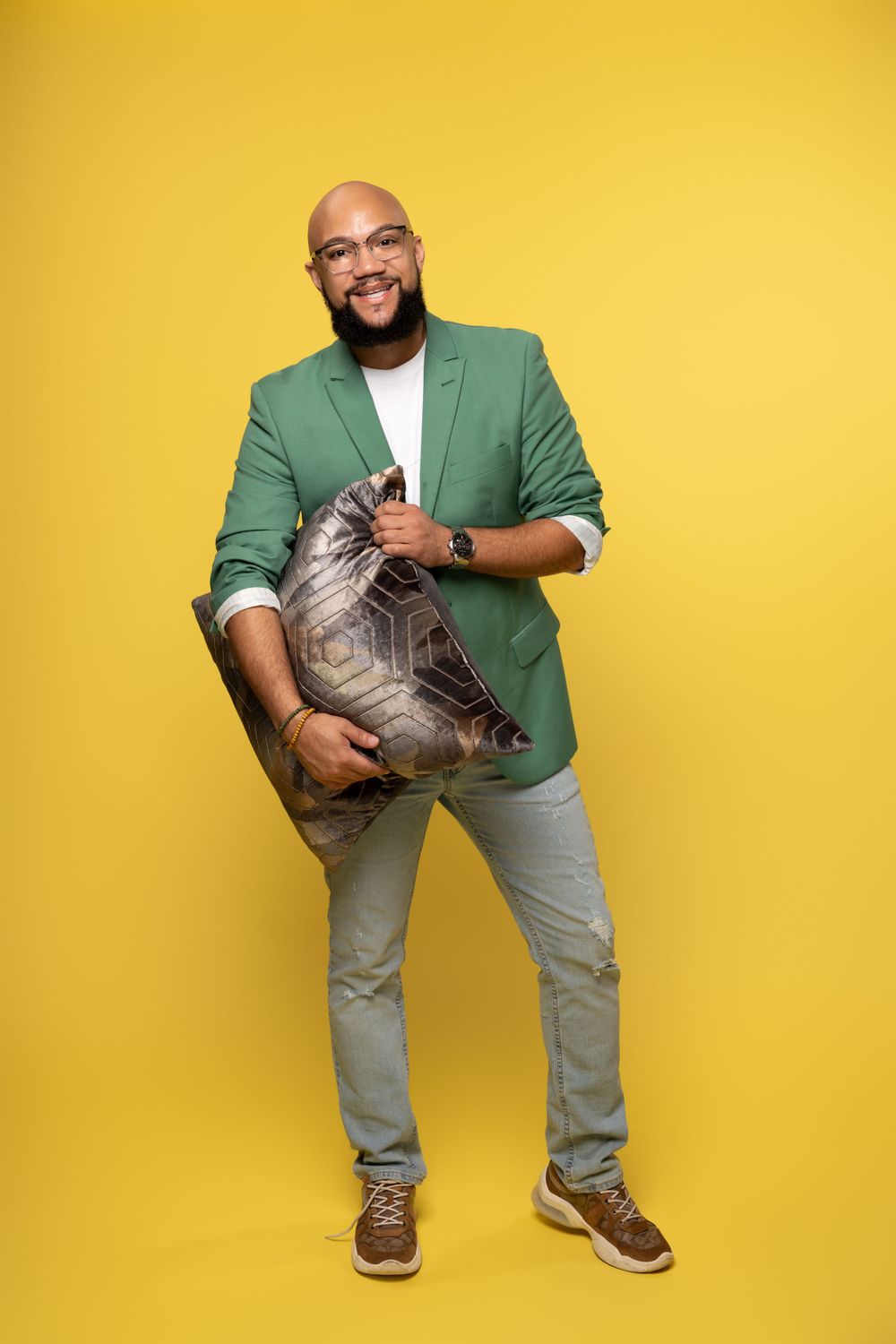 Man in green blazer and khakis poses playfully against bright yellow background.