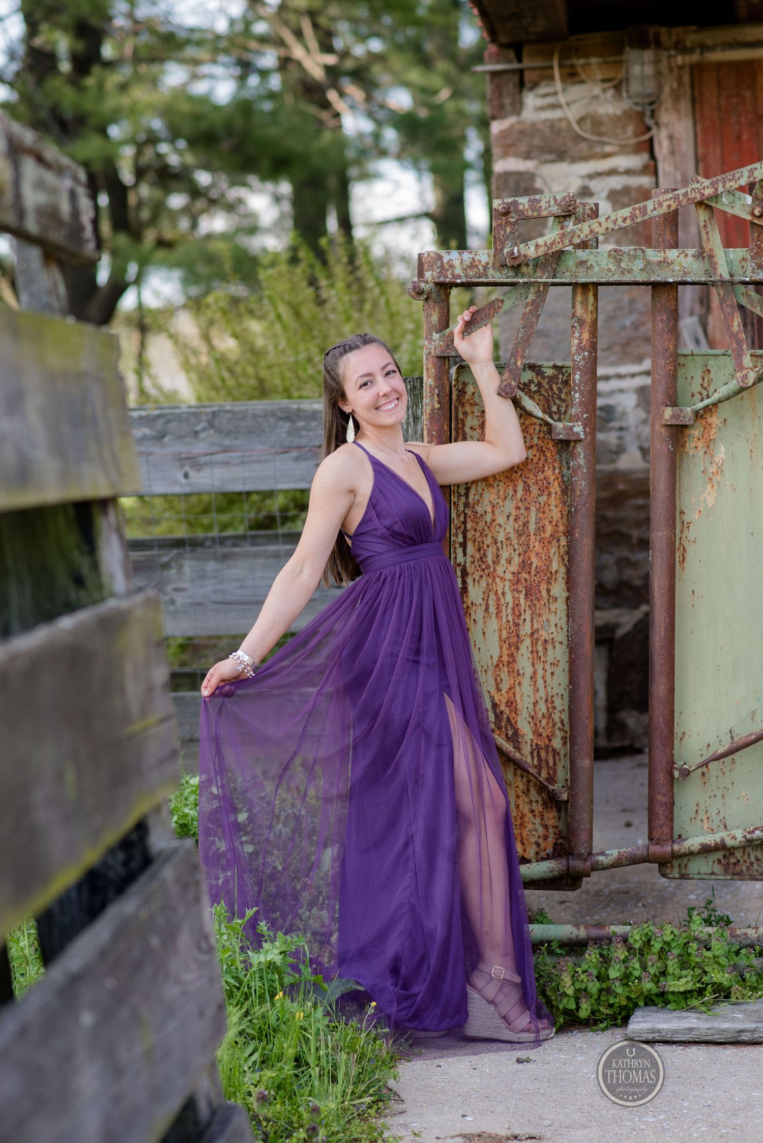 Woman in purple formal dress poses gracefully against rustic barn wall.