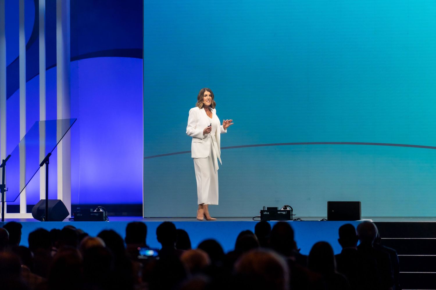 Speaker presenting on stage with blue backdrop at corporate event.