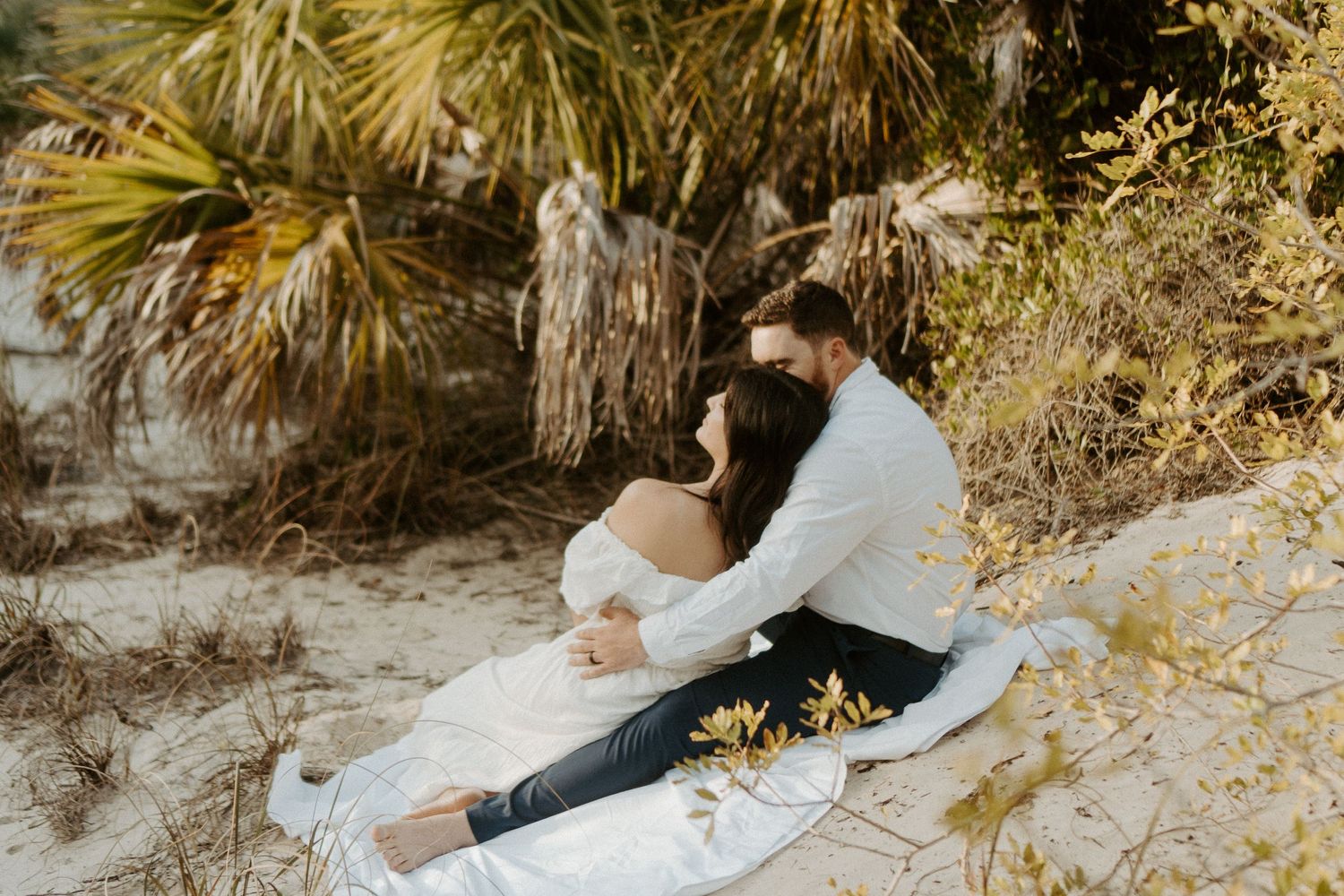 Couple sitting in the sand hugging at New Smyrna Beach Dunes at sunset