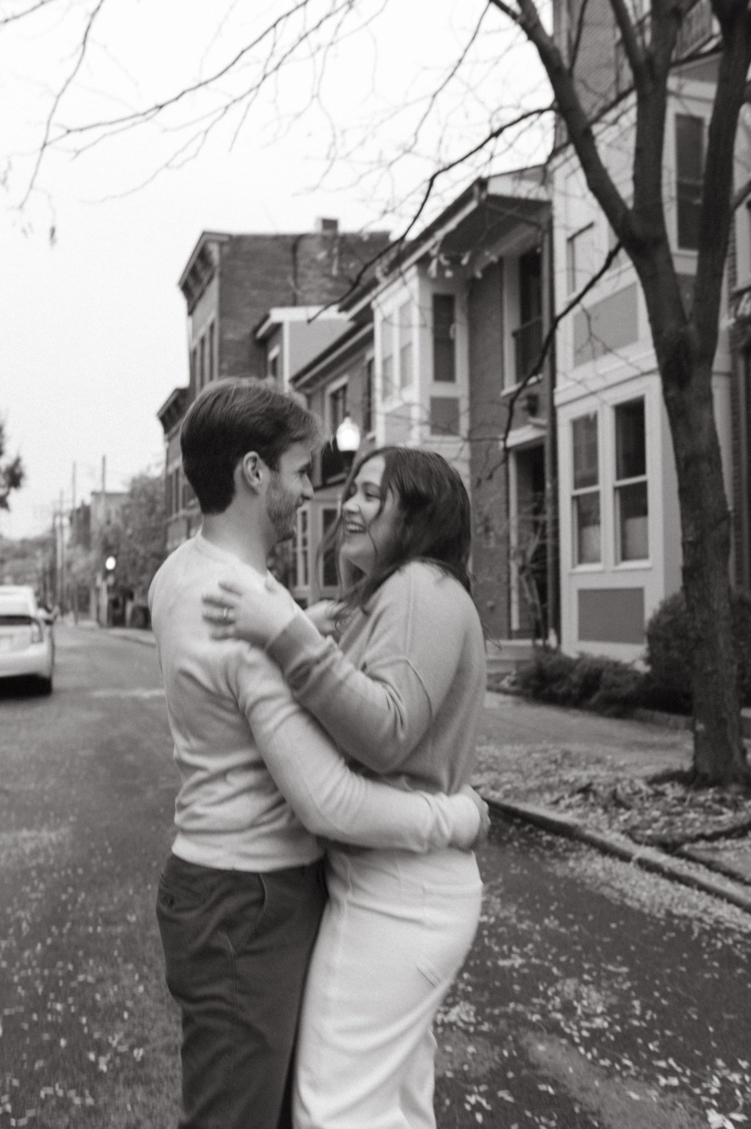 A romantic black and white photo of a couple embracing on a quiet residential street.