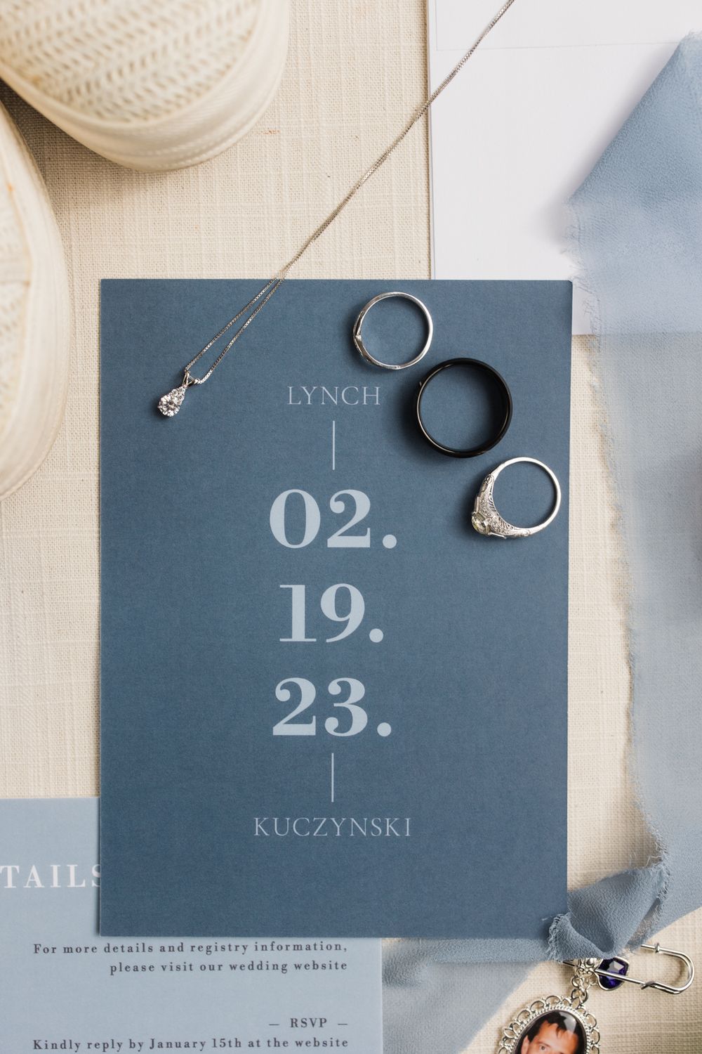 Wedding invitation with date 02.19.23 and wedding rings displayed on blue paper.