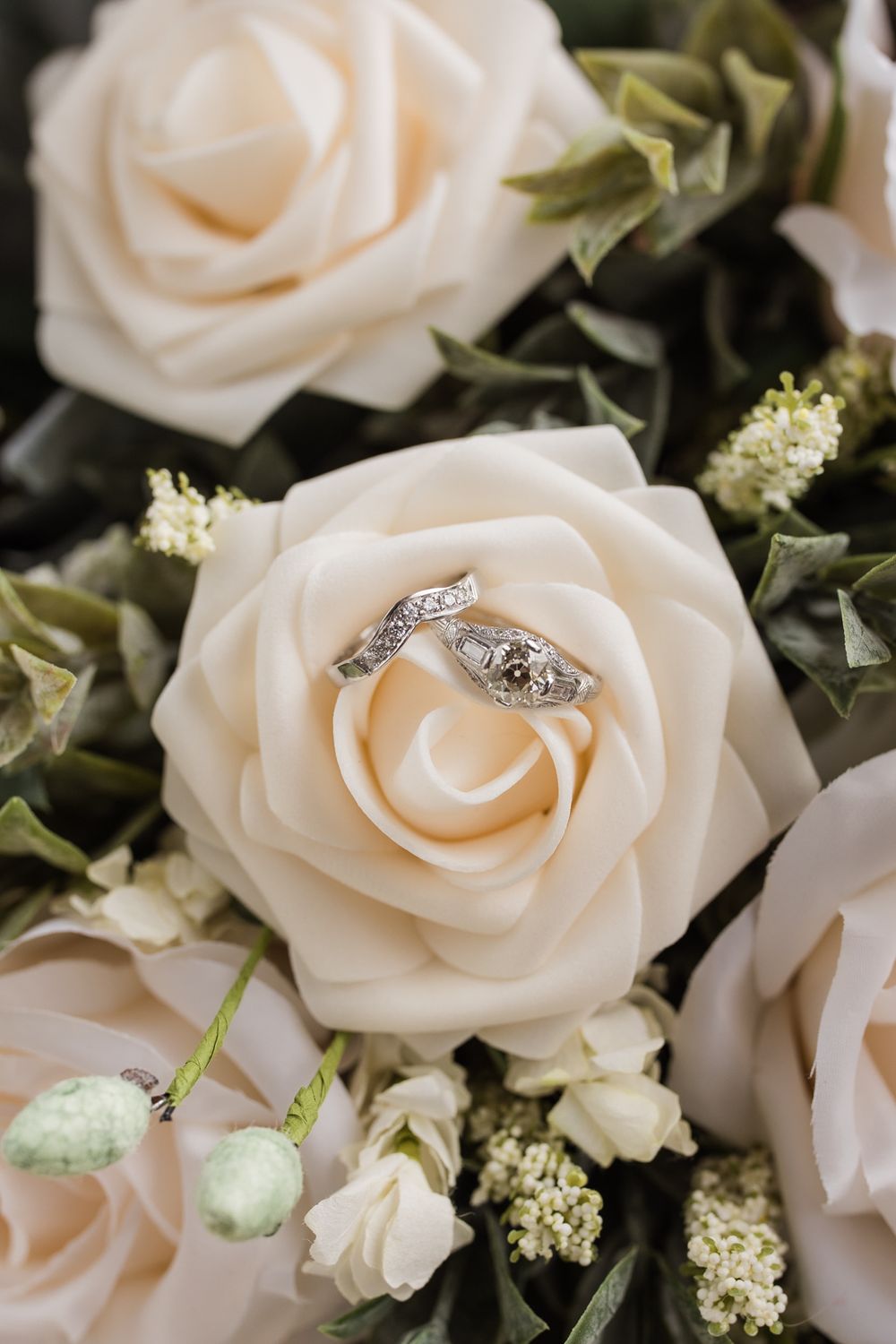 Diamond wedding rings nestled in cream roses with green foliage.