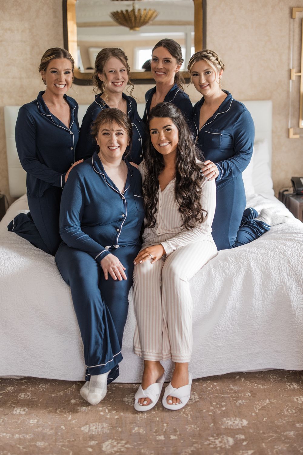 Bridal party in navy pajamas and white slippers posing on couch.