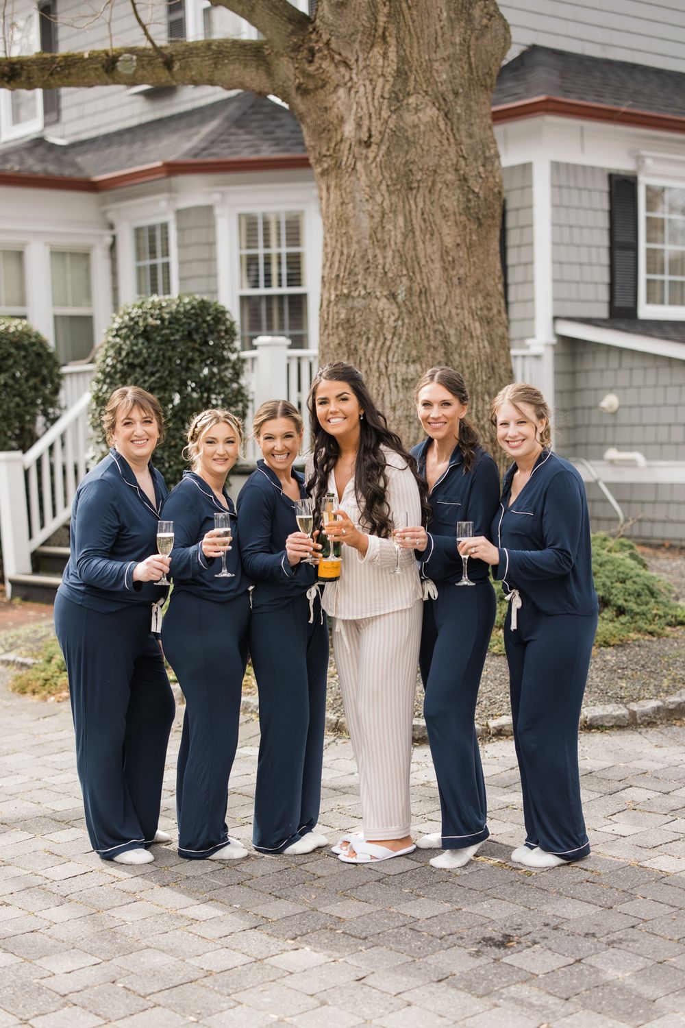 Wedding party holding champagne glasses while posing outside a house.
