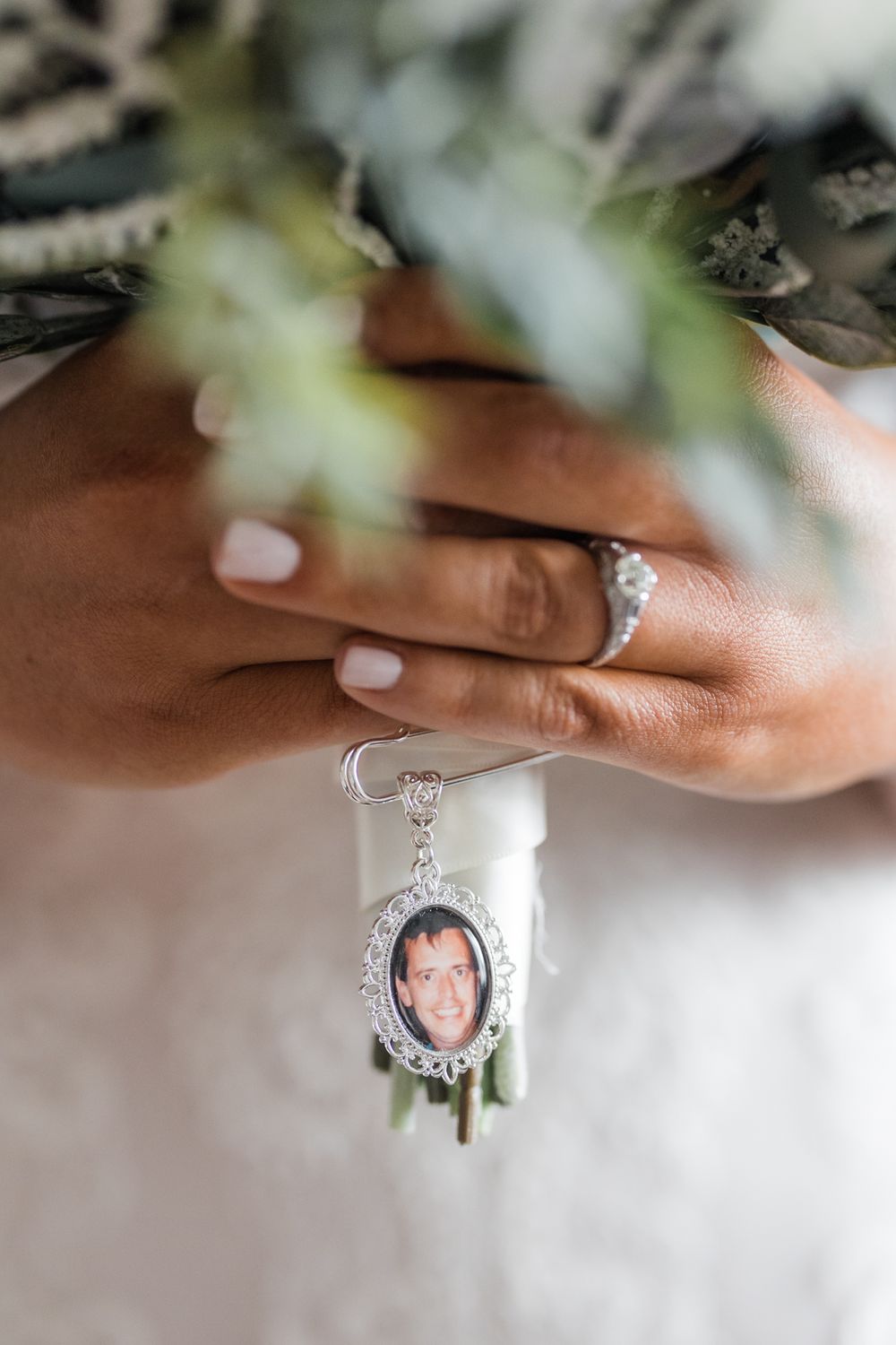 Close-up of engagement ring and sentimental photo charm on bouquet.