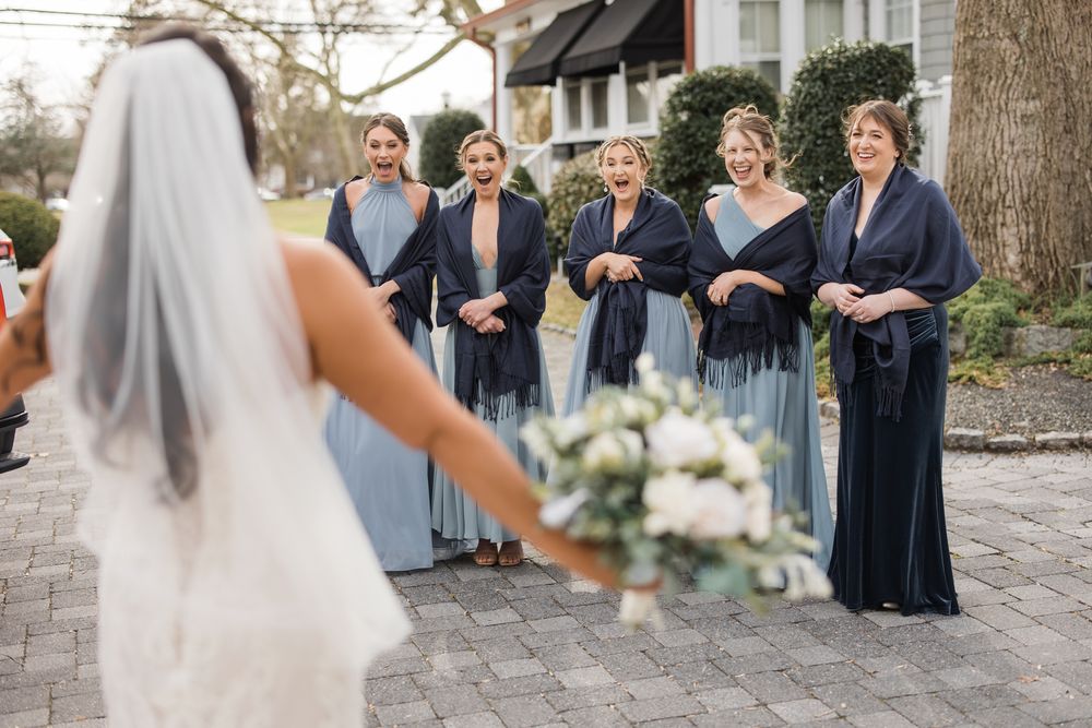 Bridesmaids in navy blue dresses stand together as bride shows her bouquet on a stone pathway.