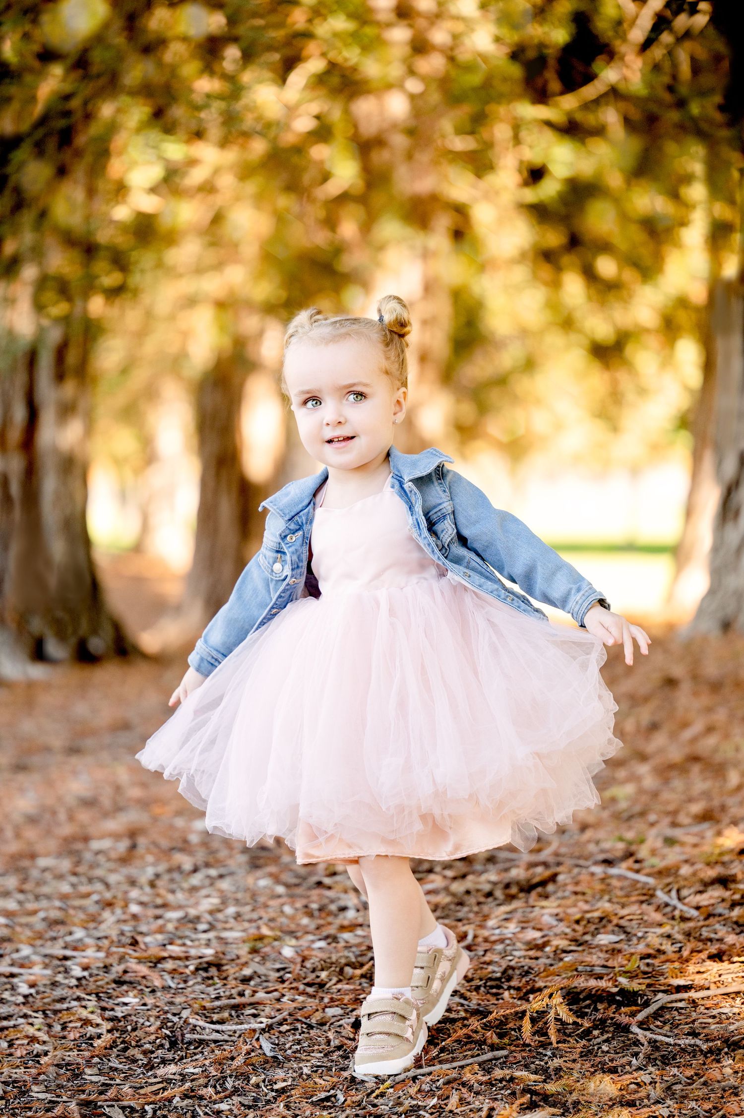 Child twirling in pink tutu and denim jacket among fallen leaves.