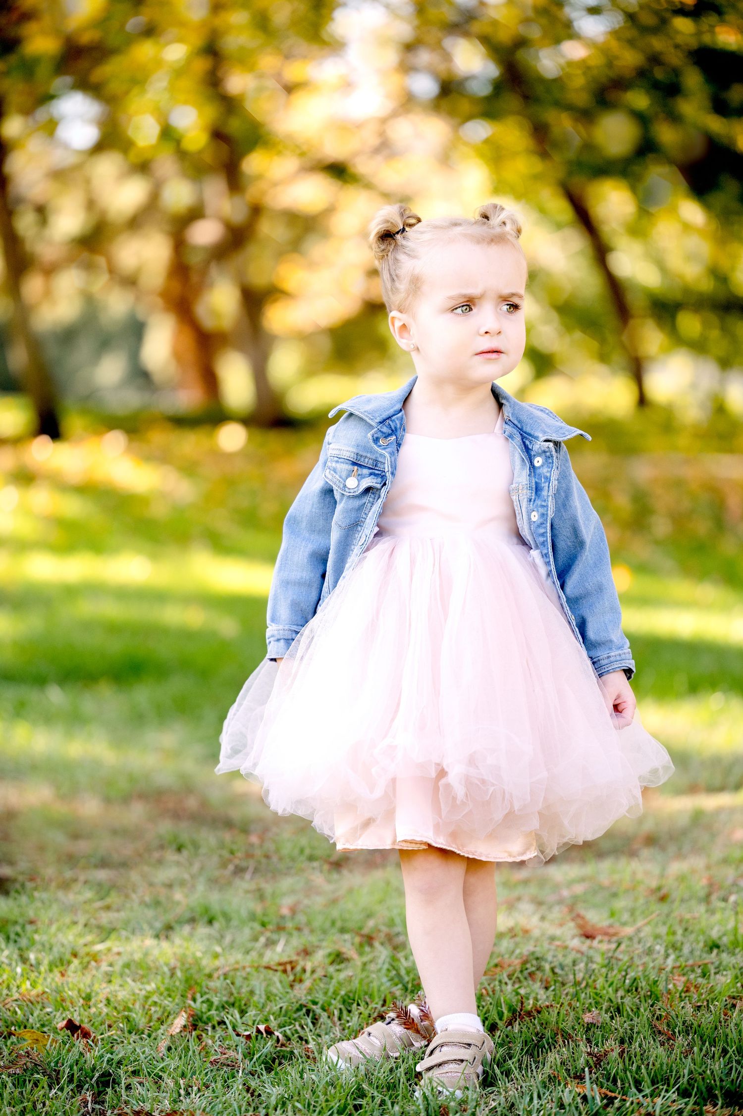 Toddler in pink tutu and jean jacket playing on grass in autumn light.