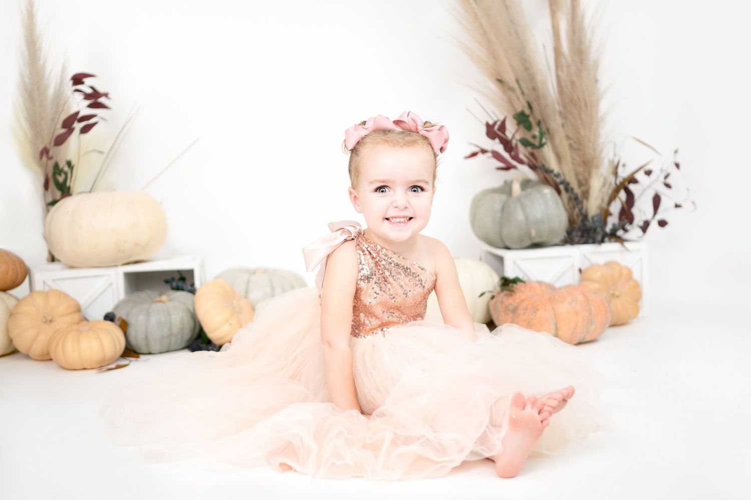 Dreamy studio portrait setup with cream pumpkins and dried botanical elements against white background.