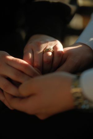 Close-up of hands holding an engagement ring in warm sunlight.
