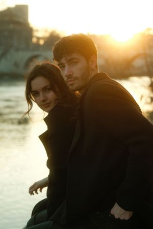 Couple in dark coats posed against golden sunset over water.