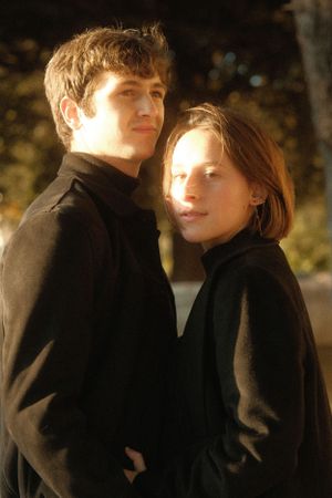 A romantic couple in black coats share an intimate moment outdoors at dusk.