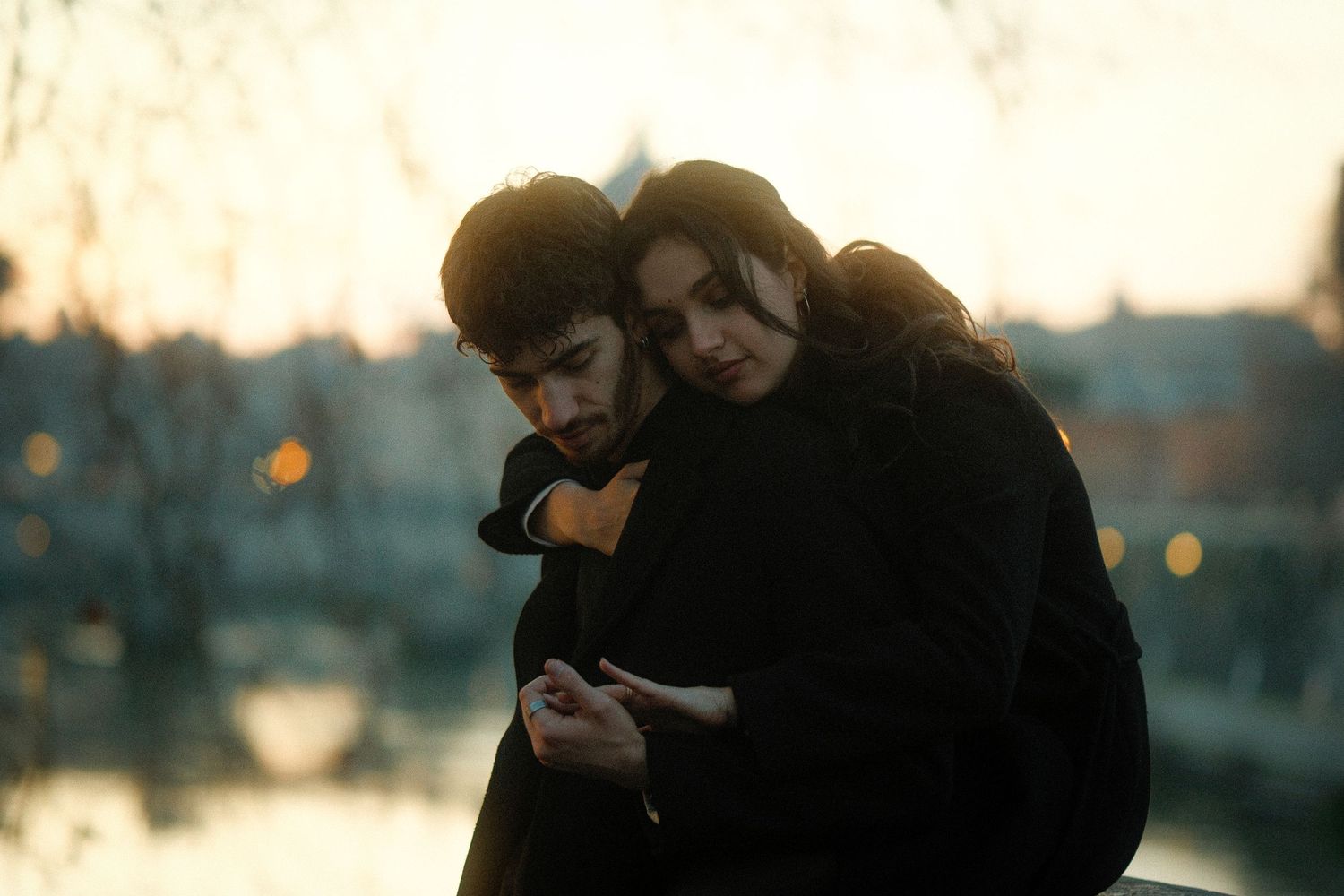 Two people sharing an intimate embrace at sunset with city lights twinkling in the background.