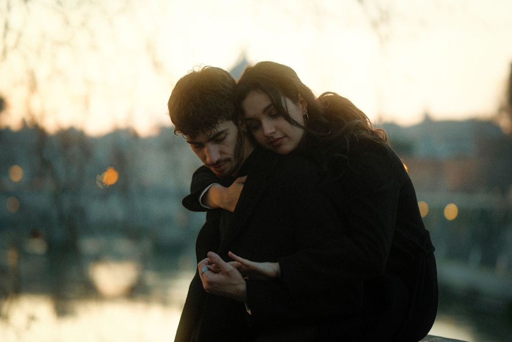 Two people sharing an intimate embrace at sunset with city lights twinkling in the background.