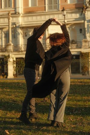 A couple dances playfully in front of a historic building on an autumn day.