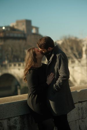 A romantic embrace against the backdrop of a historic Roman bridge at sunset.