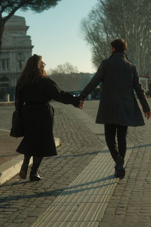 A couple walking hand in hand on a cobblestone street with historic architecture in the background.