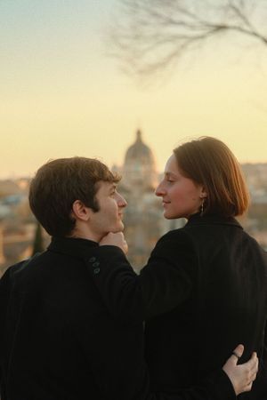 A couple embraces with the dome of St. Peter's Basilica visible in the sunset background.