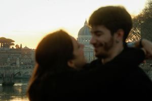 A couple embracing with St. Peter's Basilica dome visible in the golden sunset background.