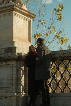 A romantic moment between two people by an ornate stone balustrade with autumn leaves in the background.