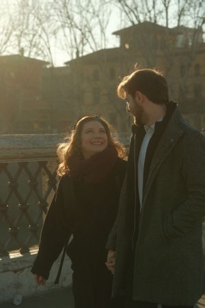 A couple sharing a joyful moment while walking along a bridge during golden hour in Rome.