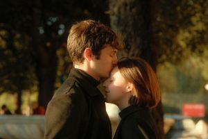 A tender moment between two people wearing dark coats in golden sunlight.