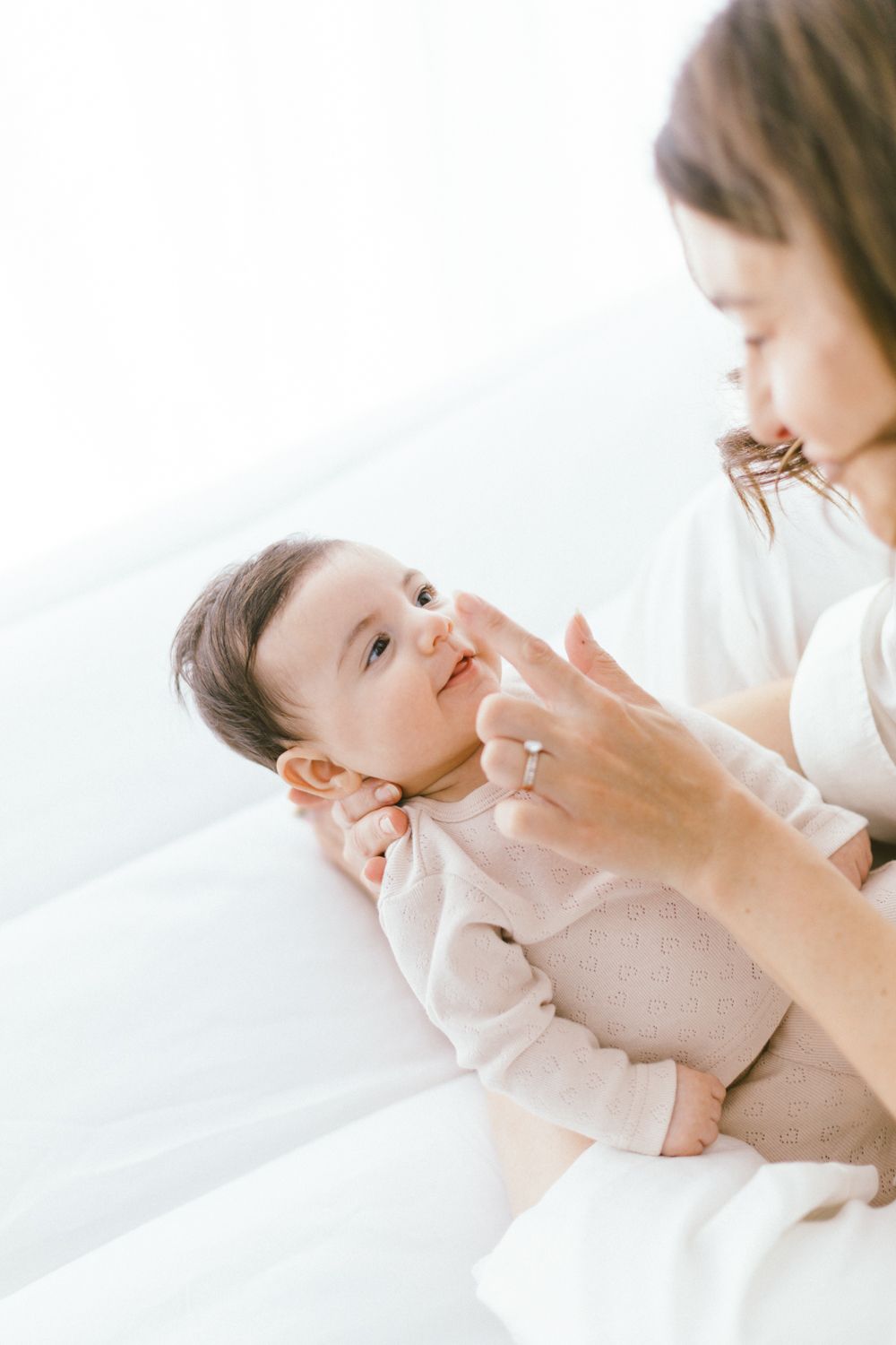 Parent caressing baby's face in soft white minimalist portrait.