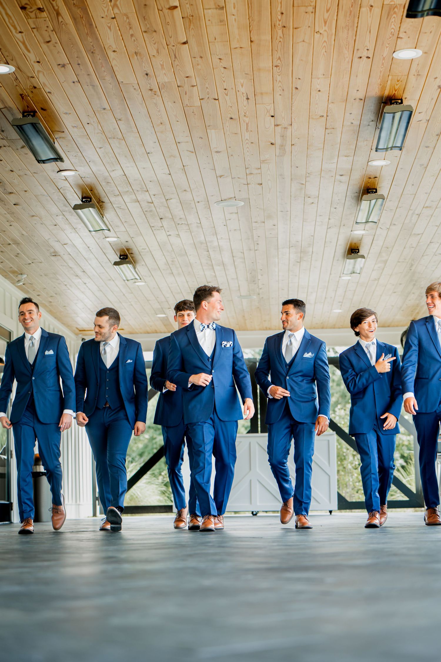 Wedding party members in navy suits line up under wooden ceiling for creative photo.