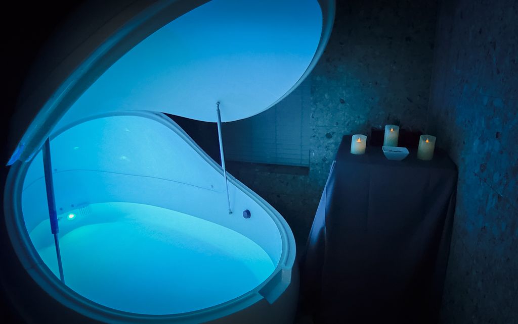 Blue-lit sensory deprivation float tank with candles in a relaxing spa environment.