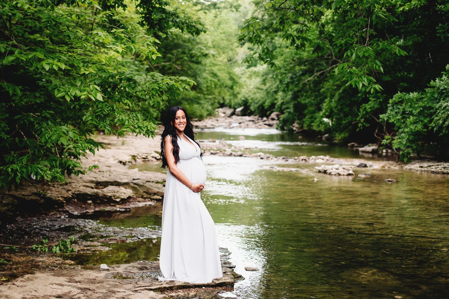 expecting woman standing on flat rocks near stream