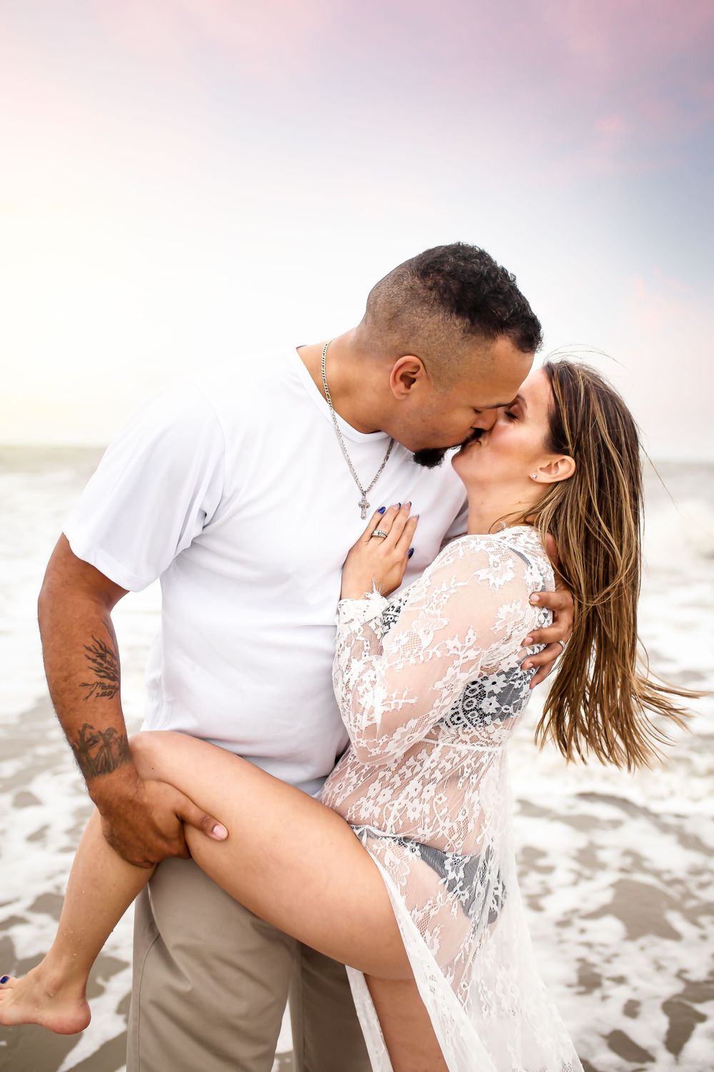 Romantic beach photo with couple in white embracing at sunset.