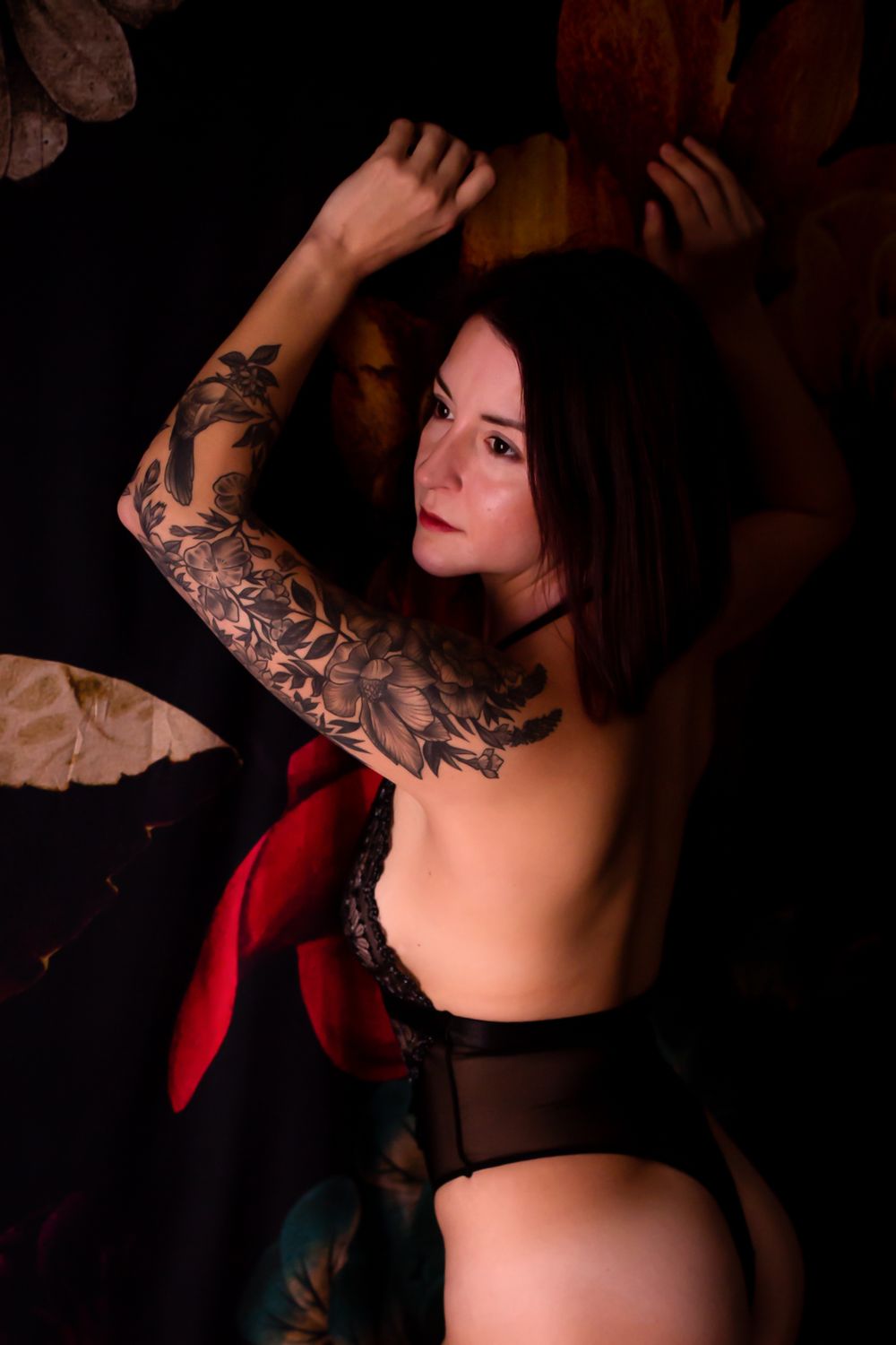 Artistic boudoir photo showing a woman with elaborate sleeve tattoo in dark lighting.