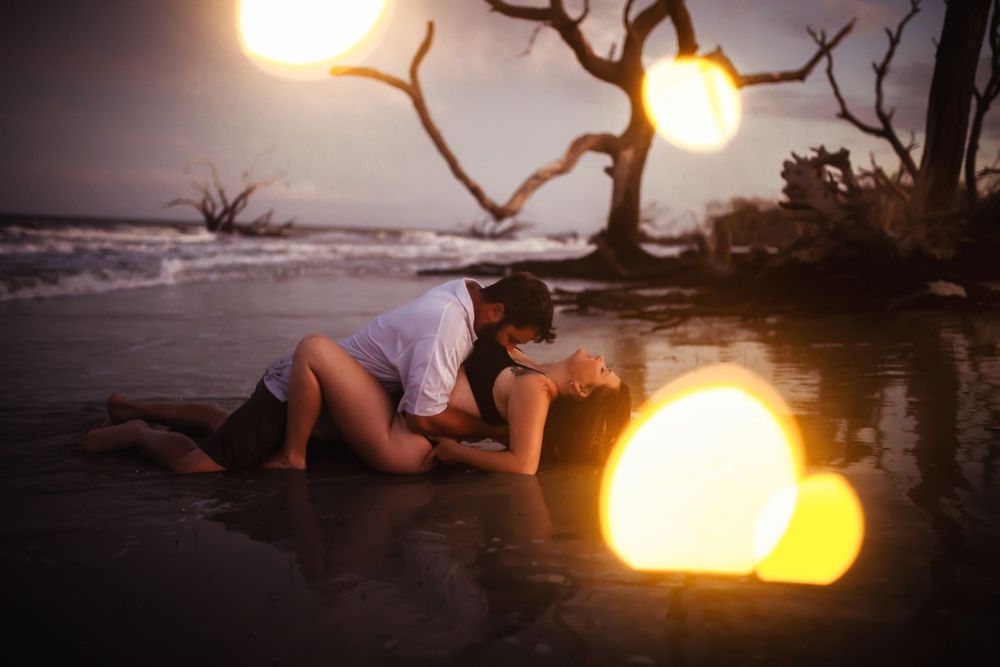 Romantic moment on beach at sunset with glowing orbs and driftwood trees.