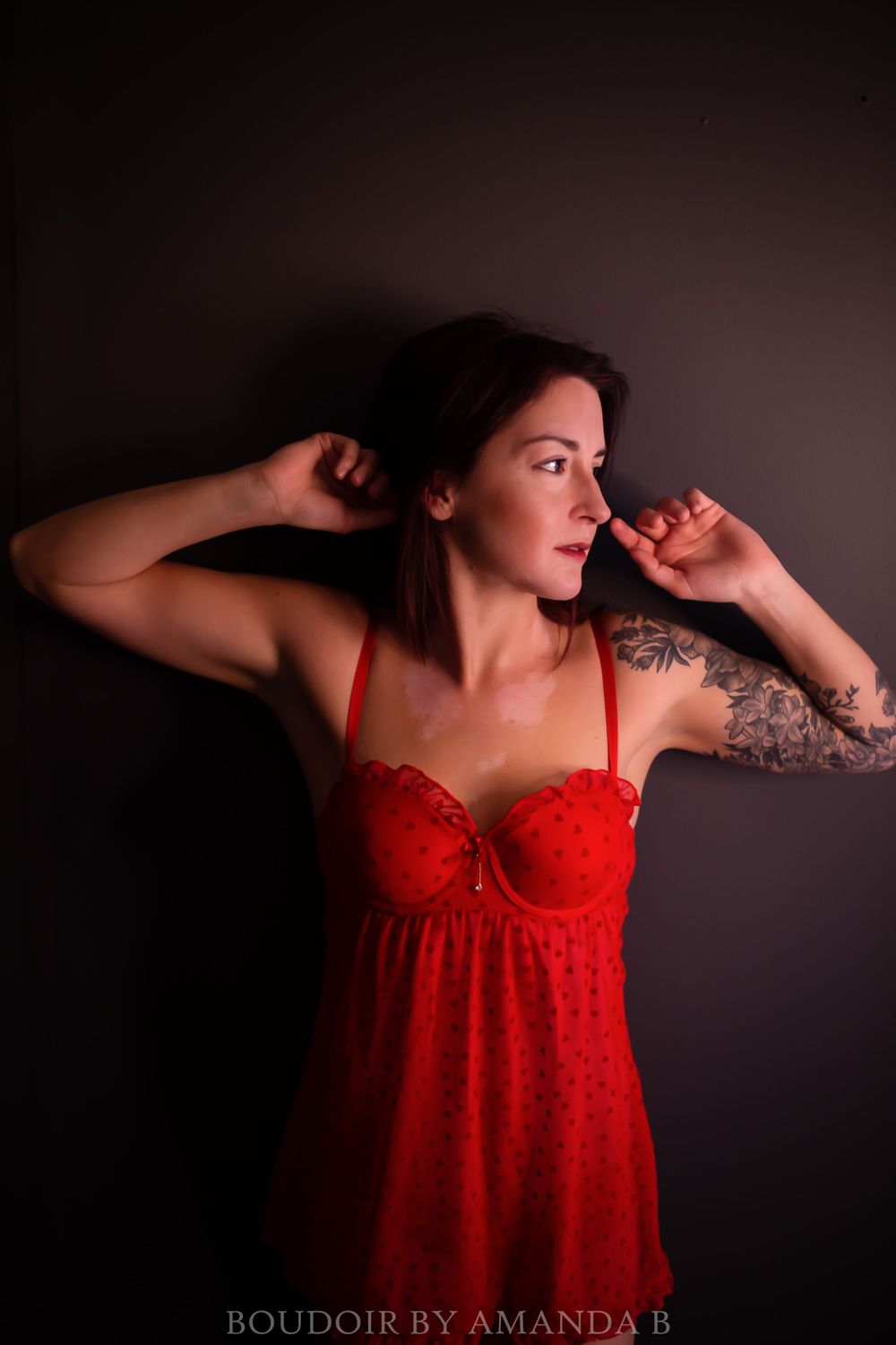 Artistic boudoir portrait in red lingerie against dark background.
