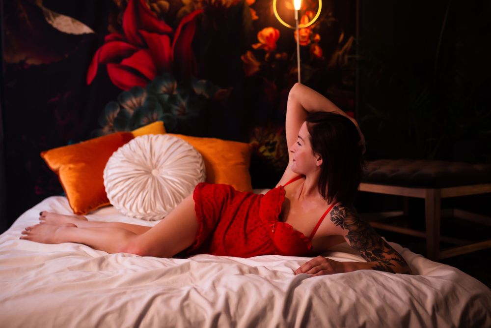 Intimate boudoir photo with red dress on bed with decorative pillows.