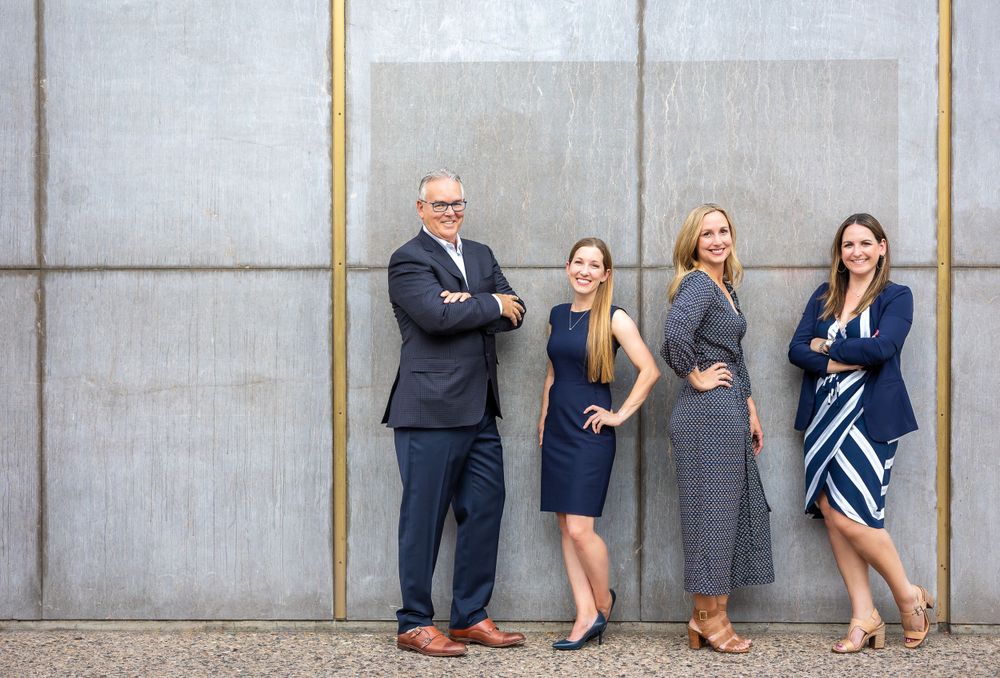 Corporate team poses confidently against concrete wall in business attire.