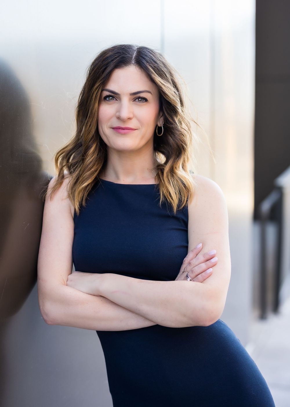 Portrait of person in navy dress with wavy hair standing confidently with arms crossed.