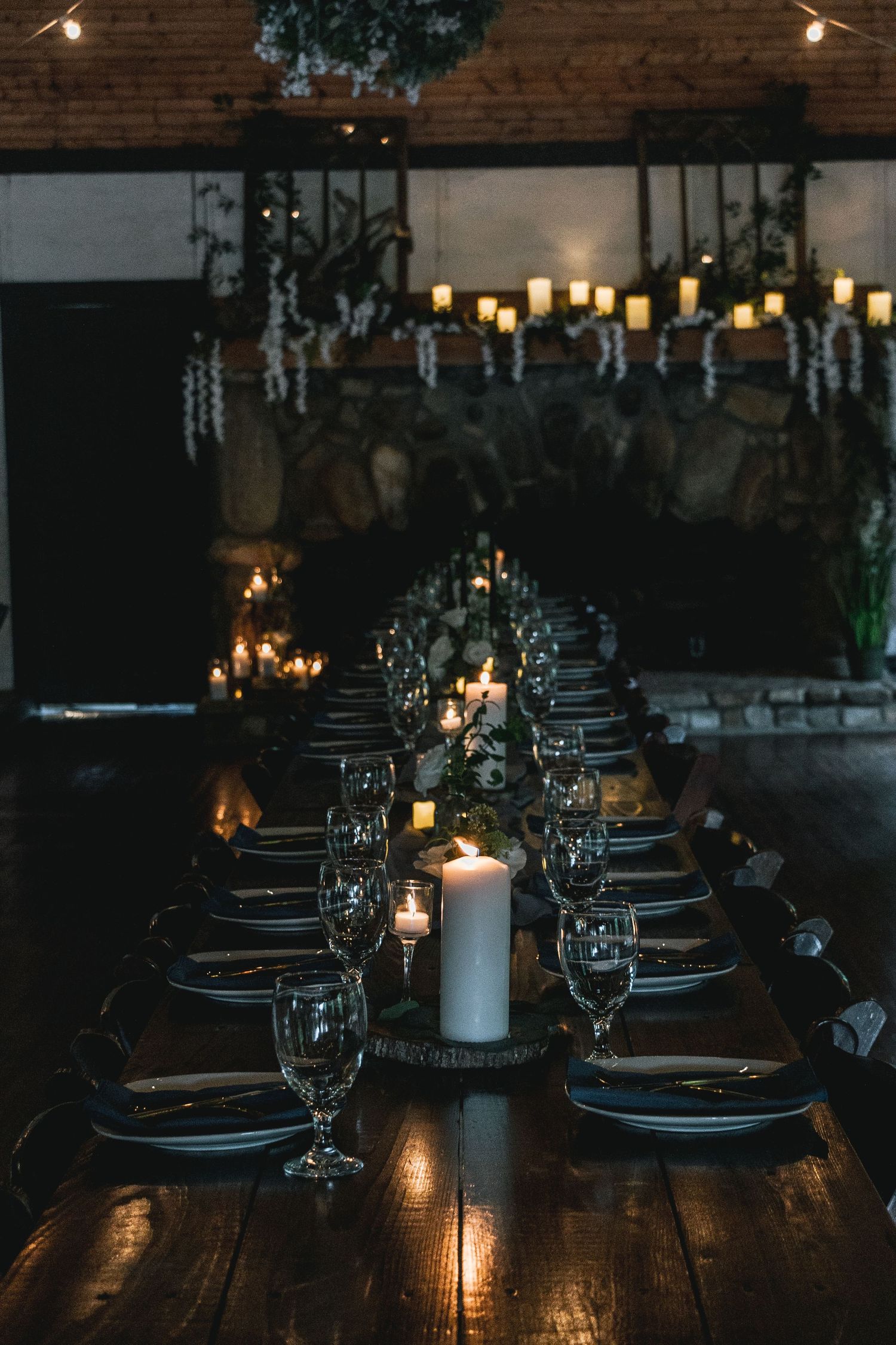 Romantic candlelit table setting with wine glasses and elegant place settings in dark rustic venue.