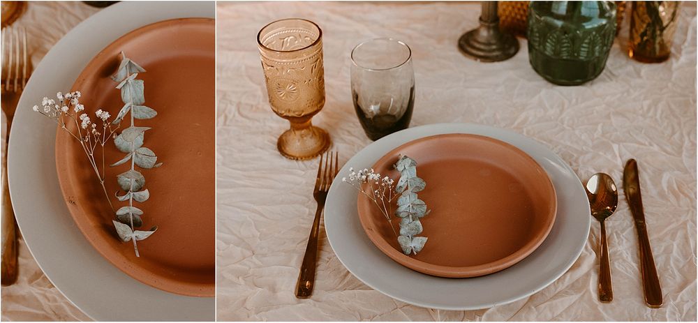 Table setting with terracotta plates, eucalyptus sprigs, and amber glassware on white linen tablecloth.
