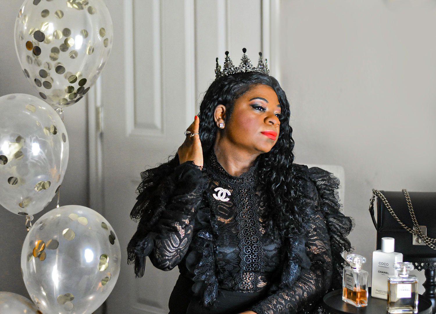 Glamorous portrait with crown and black lace against white background with gold balloons.
