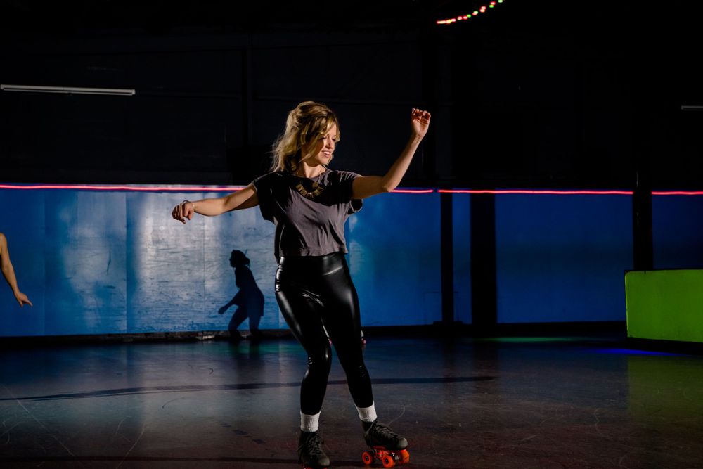 Roller skater in black performs expressive dance move on illuminated rink.