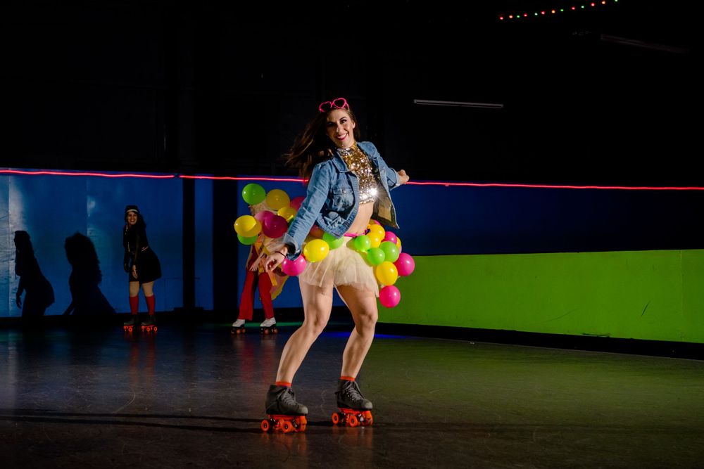 Roller skater in denim and yellow performs with balloons on dark rink.