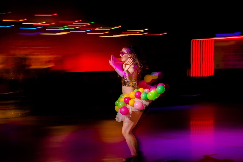 Roller skater in colorful retro outfit performs under dramatic red lighting with motion blur streaks.