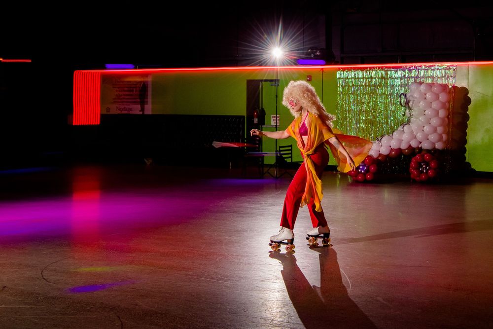 Roller skater performs on illuminated rink with colorful lighting and shadow effects.