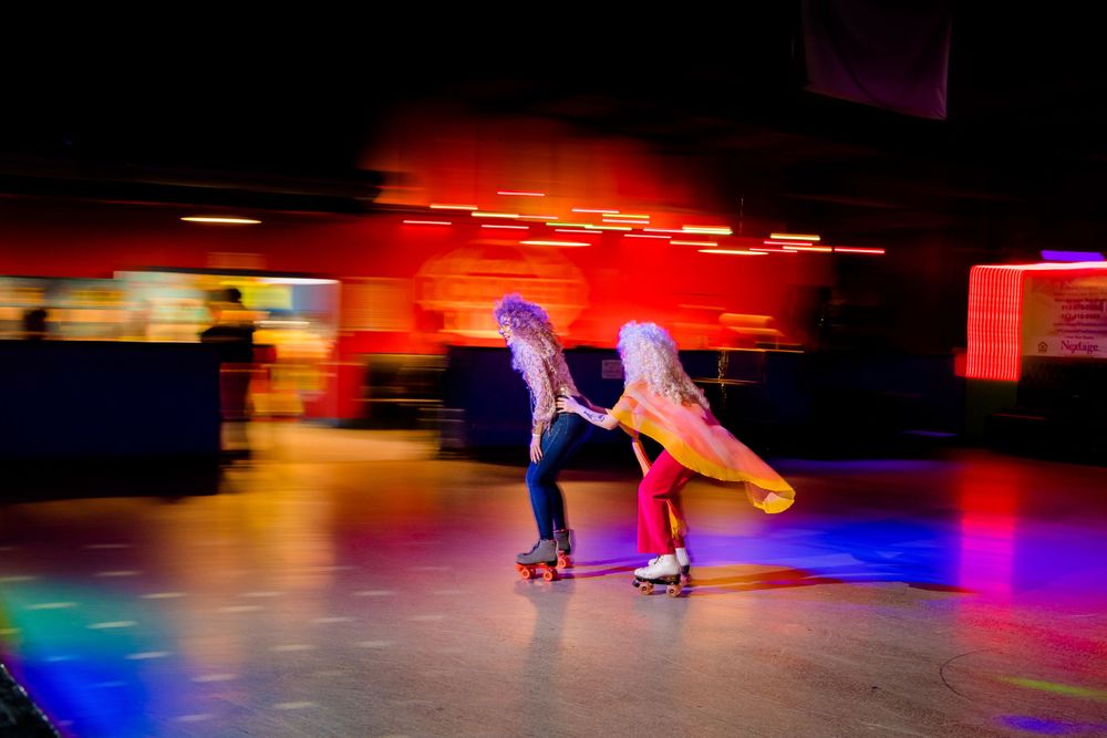 Motion-blurred roller skaters glide across colorfully lit rink with rainbow lighting effects.