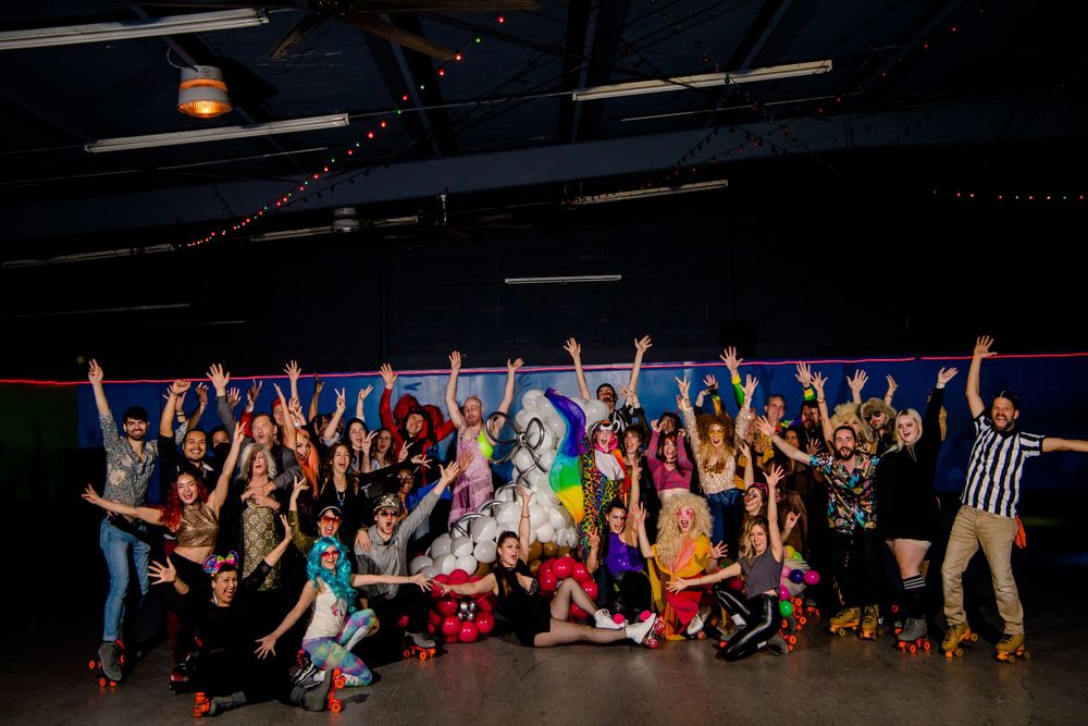 Enthusiastic group photo of roller derby team members with colorful outfits raising their arms in unison.